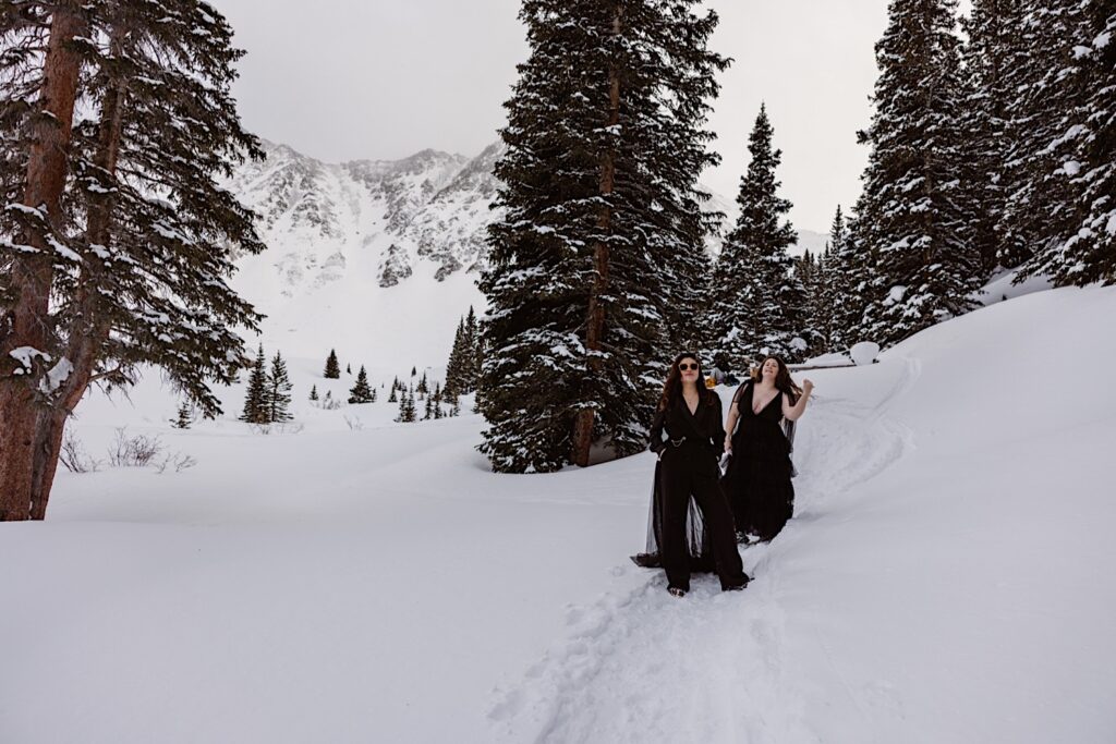 Brides in all black pose in the snowy mountains during their Colorado Elopement Ceremony. 