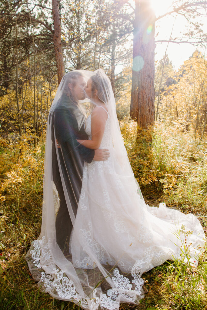 Bride and Groom kiss under the bride's veil surrounded by trees in autumn during their elopement in Breckenridge Colorado. 