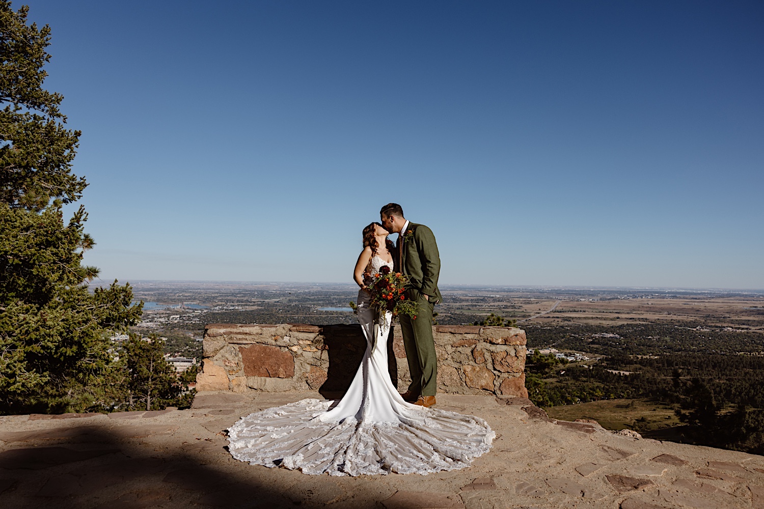 Bride with lace train kisses her groom on the edge of the amphitheater overlooking Boulder Colorado.